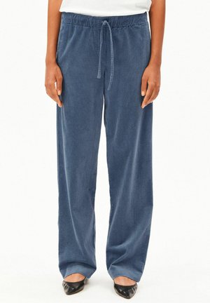 Loose blue corduroy pants with drawstring waist worn with black pointed shoes and a white top, shown from waist to feet.