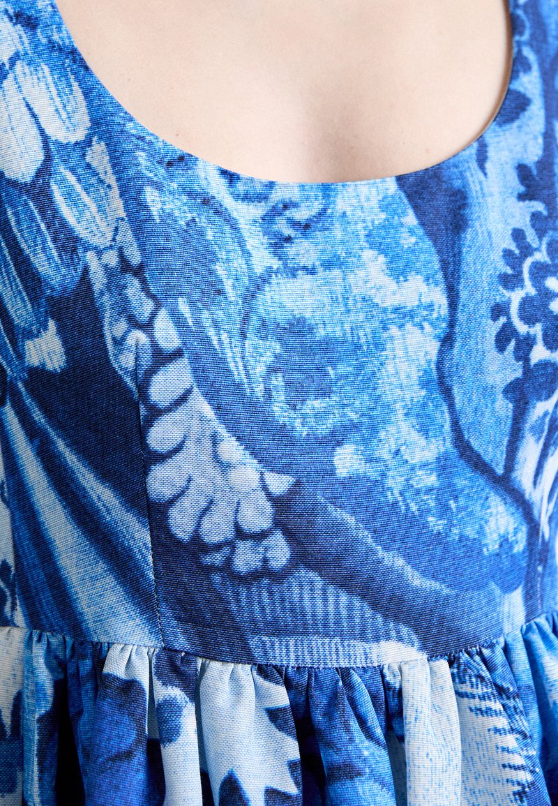 Tessuto blu a motivo floreale e astratto. Presenta un collo a giro e un design con vita arricciata. Materiale leggero e texturizzato.