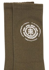 Olivengrønne sokker lavet af strikket stof med et hvidt cirkulært logodesign, der indeholder indre koncentriske cirkler og et træmotiv.