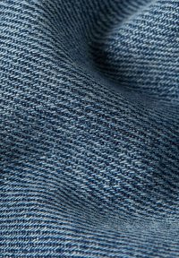 Denimtyg i varierande nyanser av blått med en texturerad väv, som har en mjuk yta och en uttalad diagonal mönster.