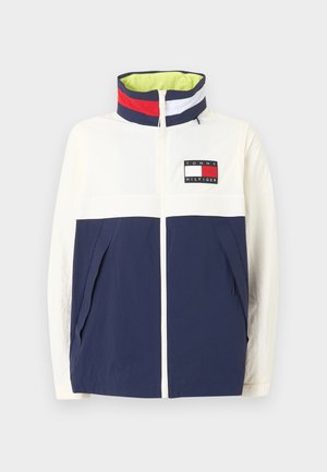 Weiße und marineblaue Jacke mit Reißverschluss vorne, hohem Kragen mit roten, weißen und marineblauen Streifen und Tommy Hilfiger-Logo auf der Brust.