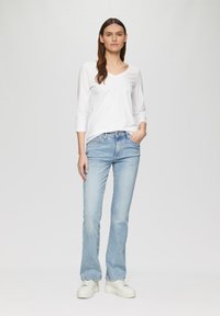 Witte V-hals lange mouwen top gecombineerd met lichtblauwe uitlopende jeans en witte platform sneakers. Eenvoudig ontwerp, geen zichtbare patronen of logo's.