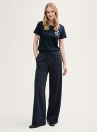 T-shirt bleu marine avec texte graphique et logo sur la poitrine gauche, associé à un pantalon large bleu marine à coupe décontractée, doté d'une taille élastique avec cordon.