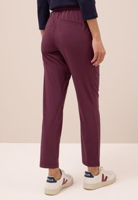Bordové kalhoty s elastickým pasem a elegantním střihem; mají zadní kapsu a jsou zkombinovány s bílými teniskami s barevnými akcenty.