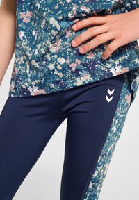 Top corto a maniche corte con motivo floreale in blu, verde e rosa; abbinato a leggings blu navy con chevron bianchi sui lati e una superficie liscia.