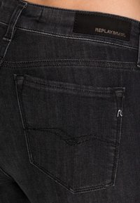 Jeans de mezclilla negra con un acabado texturizado, que cuentan con un bolsillo trasero, costuras en contraste y un parche de cuero con la marca en la cinturilla.