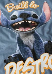 Niebieska postać kreskówkowa z dużymi uszami i oczami, pokazująca zęby. Napis "Built to Destro" na pomarańczowo. Miękka tekstura tkaniny, uśmiechnięta mina.
