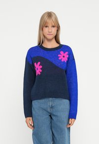 Blue and navy knit sweater featuring pink floral patterns and a wavy design. Ribbed crew neckline and cuffs, soft texture, casual fit.