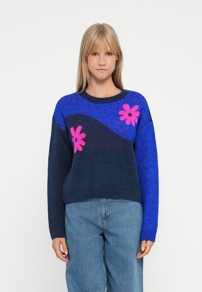 Blue and navy knit sweater featuring pink floral patterns and a wavy design. Ribbed crew neckline and cuffs, soft texture, casual fit.
