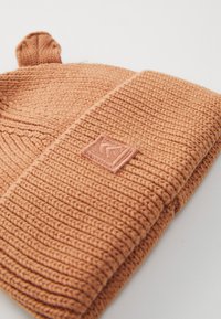 Pletena narančasta beanies kapa s preklopom, koja ima suptilan teksturirani uzorak i malu tkanu oznaku s logom sa strane.
