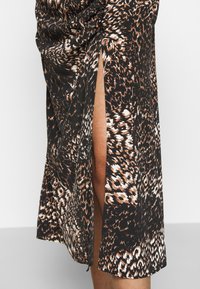 Svart och brun leopardmönstrad kjol med en hög sidoklyvning. Har samlad detaljering vid midjan och en slät textur.