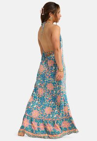 Maxi jurk in een blauw bloemenpatroon, met een open rug, halternek met strik en een flared zoom met roze accenten en franje.