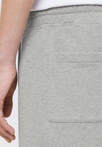 Grijze katoenen joggingbroek met een zak aan de zijkant, met een zachte textuur en een eenvoudig ontwerp, afgebeeld naast een hand.