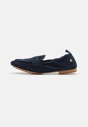 Mocassins en daim bleu marine avec une sangle cousue, bout rond et semelle texturée. Présentent un accent en or sur le talon.