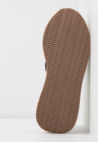 Semelle de chaussure en caoutchouc marron avec un motif ondulé, vue de dessous sur fond blanc.
