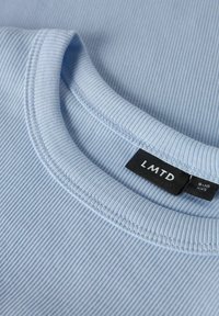Lichtblauwe geribbelde stof t-shirt met een ronde halslijn, zichtbare stiksels en een zwart etiket met "LMTD" en maatdetails.