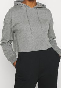 Cropped grey hoodie in soft fabric, featuring a drawstring hood and long sleeves. Paired with black pants, showing side pockets.