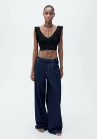 Musta neule crop-top, jossa on röyhelöhihoja, yhdistettynä korkeavyötäröisiin, leveälahkeisiin tummiin farkkuihin, joissa on revitty helma.