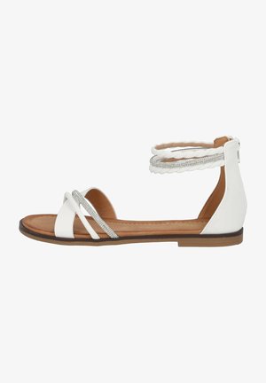 Die weiße flache Sandale verfügt über einen geflochtenen Knöchelriemen mit silbernen Akzenten und ein überkreuztes Riemendesign. Die Sohle ist braun, was einen Kontrast schafft.