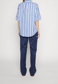 Camicetta a maniche corte a righe verticali blu e bianche con orlo curvo, abbinata a pantaloni a gamba larga blu navy scuro con tasche laterali.