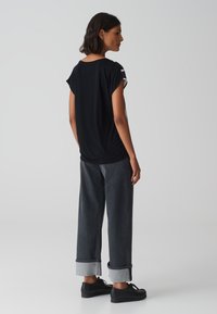 Zwart T-shirt met korte mouwen en een relaxed fit, gecombineerd met donkerdenim wijde broek met omgeslagen zoom en zwarte schoenen.