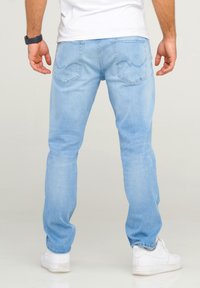 Light blue jeans made of denim, featuring a straight-leg design, two back pockets, and subtle stitching details. Worn with white sneakers.