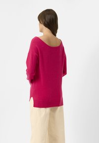 Fuchsian, oversize tröja med vid halsringning, mjuk textur och ribbade ärmslut. Har sidofickor i fållen för en avslappnad passform.