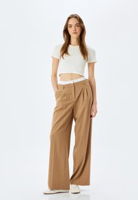 Creme cropped top parret med højtaljede, lysebrune vidde bukser med plisseret design og en hvid elastisk talje. Hvide sneakers.