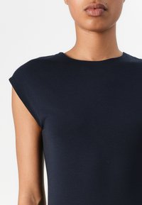 Σκούρο μπλε κοντομάνικο μπλουζάκι με στρογγυλή λαιμόκοψη, κατασκευασμένο από λείο, ελαστικό υλικό. Διαθέτει μανίκια στις ώμους και εφαρμοστή γραμμή.