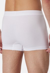 Weiße Baumwoll-Boxershorts mit glatter Textur, enganliegendem Design und weichem elastischen Bund. Sie verfügen über eine kurze Beinlänge und minimalen Nähten.