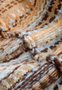 Strickstoff in warmen Tönen von Braun, Beige und Hellblau, mit einem strukturierten Muster und rötlich-braunen Akzenten sowie weicher, flauschiger Wolle.