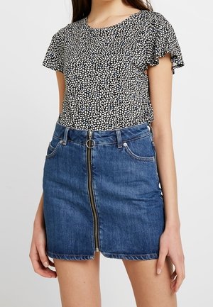 Top de manga corta con patrón en blanco y negro y bordes con volantes, combinado con una falda de mezclilla azul que tiene una cremallera frontal y cinco bolsillos.