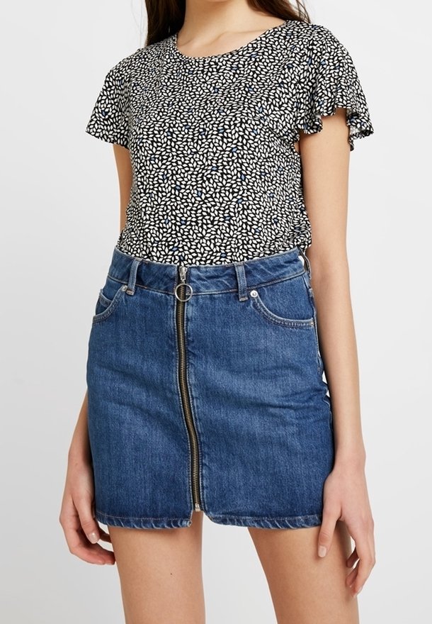 Černobílý vzorovaný top s krátkým rukávem a volánkovými okraji v kombinaci s modrou džínovou sukní s předním zipem a pěti kapsami.