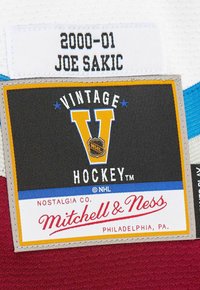Vintage hockey jersey label with a yellow "V" logo, black fabric background, red and blue accents, and text detailing player Joe Sakic, year 2000-01.