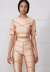 Top crop bege e leggins com detalhes em vermelho em cruz. Tecido liso e elástico; mangas curtas; design que expõe a barriga.