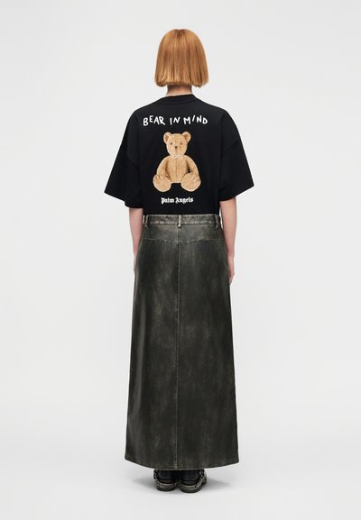 Μαύρο oversized t-shirt με γραφικό αρκουδάκι και κείμενο στην πλάτη, σε συνδυασμό με μια σκούρα, υφασμάτινη μακριά φούστα με ζώνη στη μέση.