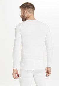 Haut de sport blanc à manches longues en tissu extensible. Présente un design ajusté, une texture lisse et des coutures plates.