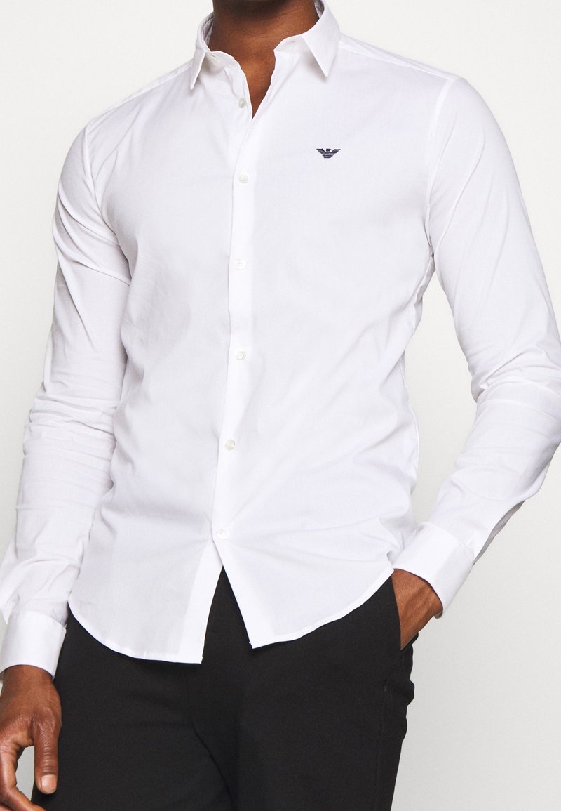 Valkoinen nappikauluspaida, jossa on slim fit -leikkaus, pitkät hihat ja pieni brodeerattu logo vasemmassa rinnassa. Sileä puuvillakangas.