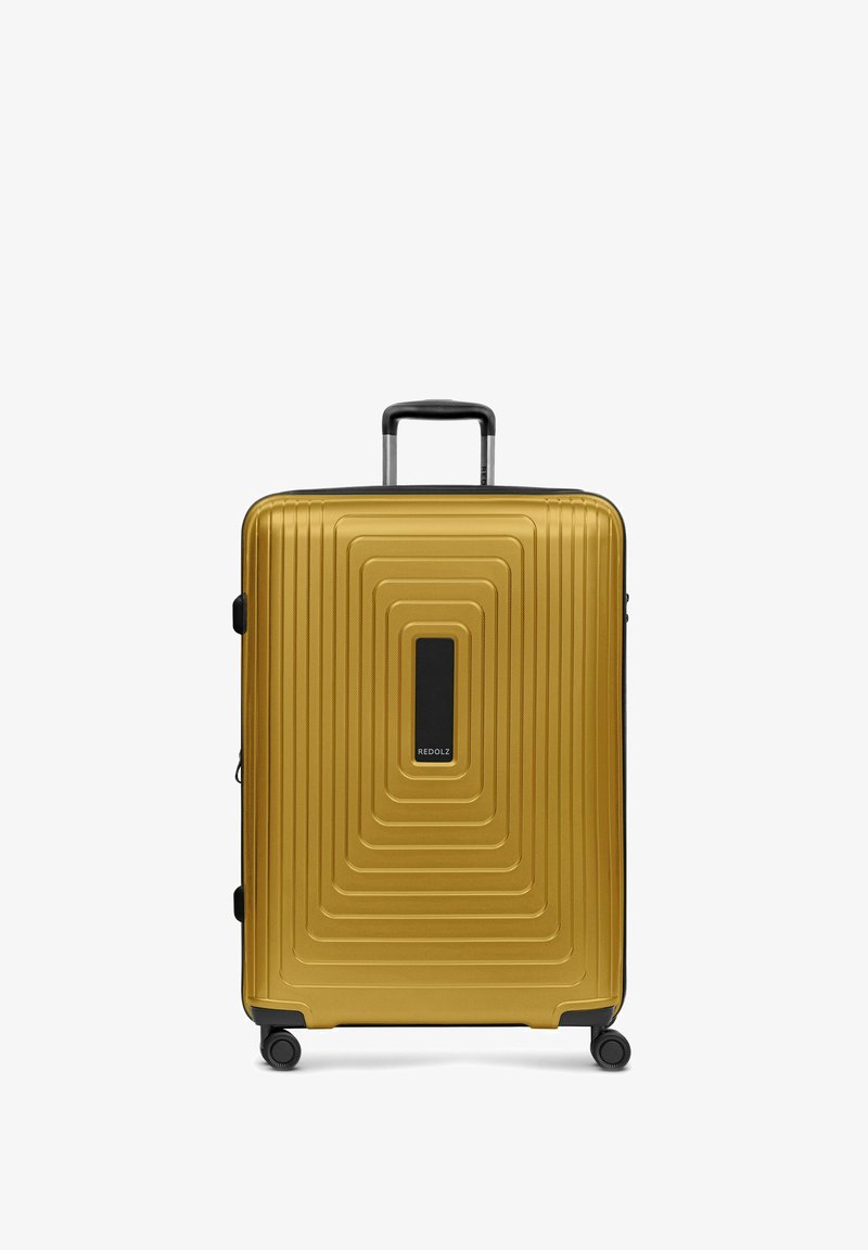Valise coque rigide dorée avec quatre roues noires, poignée télescopique déployée et motif rectangulaire géométrique sur la surface avant.