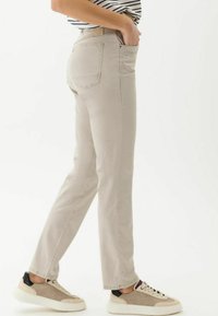 Beige gerade geschnittene Jeans aus Baumwolle, mit klassischen Taschen, dezenten Nähten und kombiniert mit mehrfarbigen Sportschuhen.