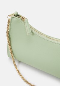 Sac à main textured vert clair avec fermeture éclair dorée et bandoulière en chaîne dorée sur fond blanc.