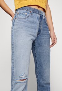 Lichtblauwe denim jeans met een relaxte pasvorm, met verwerkte details en een gescheurde knie. Afgewerkt met oranje stiksels en metalen klinknagels.
