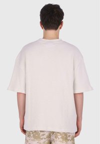 Lys beige oversized kortærmet T-shirt med struktureret ribbet stof, der har en rund halsudskæring og en afslappet pasform, parret med mønstrede shorts.