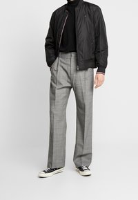 Sort bomberjakke med røde og hvide detaljer, tætsiddende turtleneck, grå plaid højtaljede bukser og sorte sneakers med hvide såler.