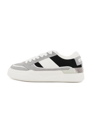 Sneaker in suede grigio e mesh con dettagli neri e bianchi. Presenta una suola testurizzata, lacci bianchi e un dettaglio posteriore semitrasparente.