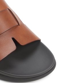 Brune læder slide-sandal med en bred strop og udskæringsdesign, der har en sort gummisål med en struktureret overflade.