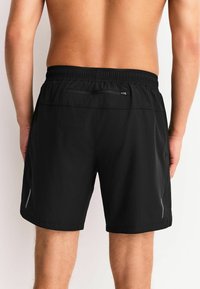 Schwarze Sportshorts mit einem elastischen Bund, hinten mit einer Reißverschlusstasche und reflektierenden Akzenten an den Seiten.
