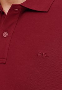 Bordowa koszulka polo o teksturowanym splocie, z trzema guzikami z przodu i haftowanym logo na klatce piersiowej.