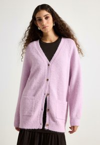 Lyserød, fluffy cardigan med V-hals, forreste knaplukning, to store lommer og lange ærmer med ribbede manchetter og kant.