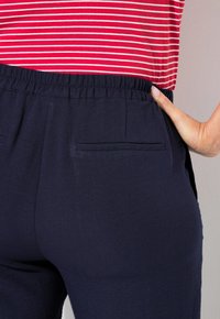 Marinblå byxor med resårmidja och två bakfickor, med en slät textur. Rödrandig topp delvis synlig vid midjan.